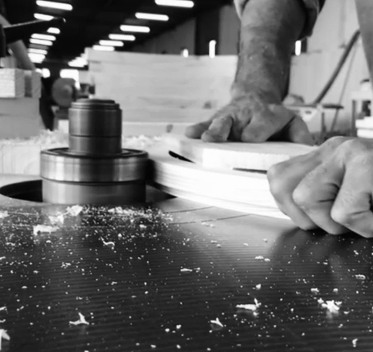 Black-and-white close-up of a craftsman's hands shaping timber at a machine